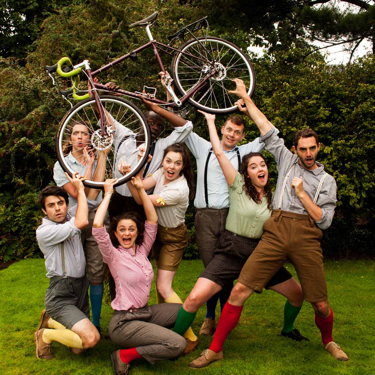 8 people holding up a bike dressed in period costumes
