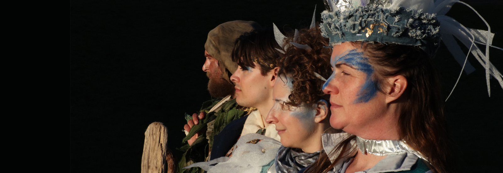 Four characters from The Tempest in costume looking out to the left of the image