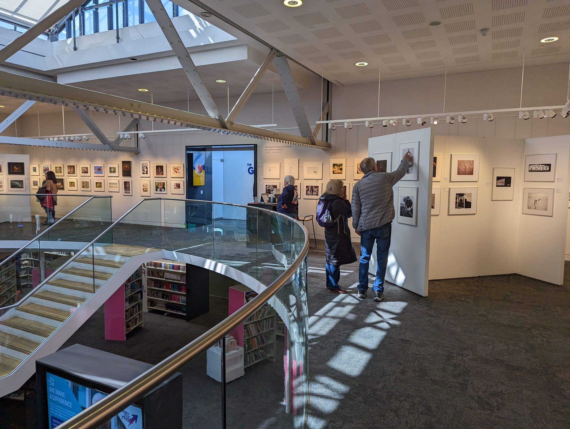 Photos in frames on a white wall around a gallery with people looking at them